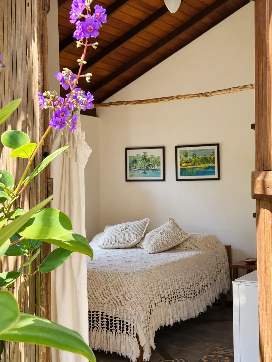 Entrada do Bangalô 7 com flores em primeiro plano e vista da cama