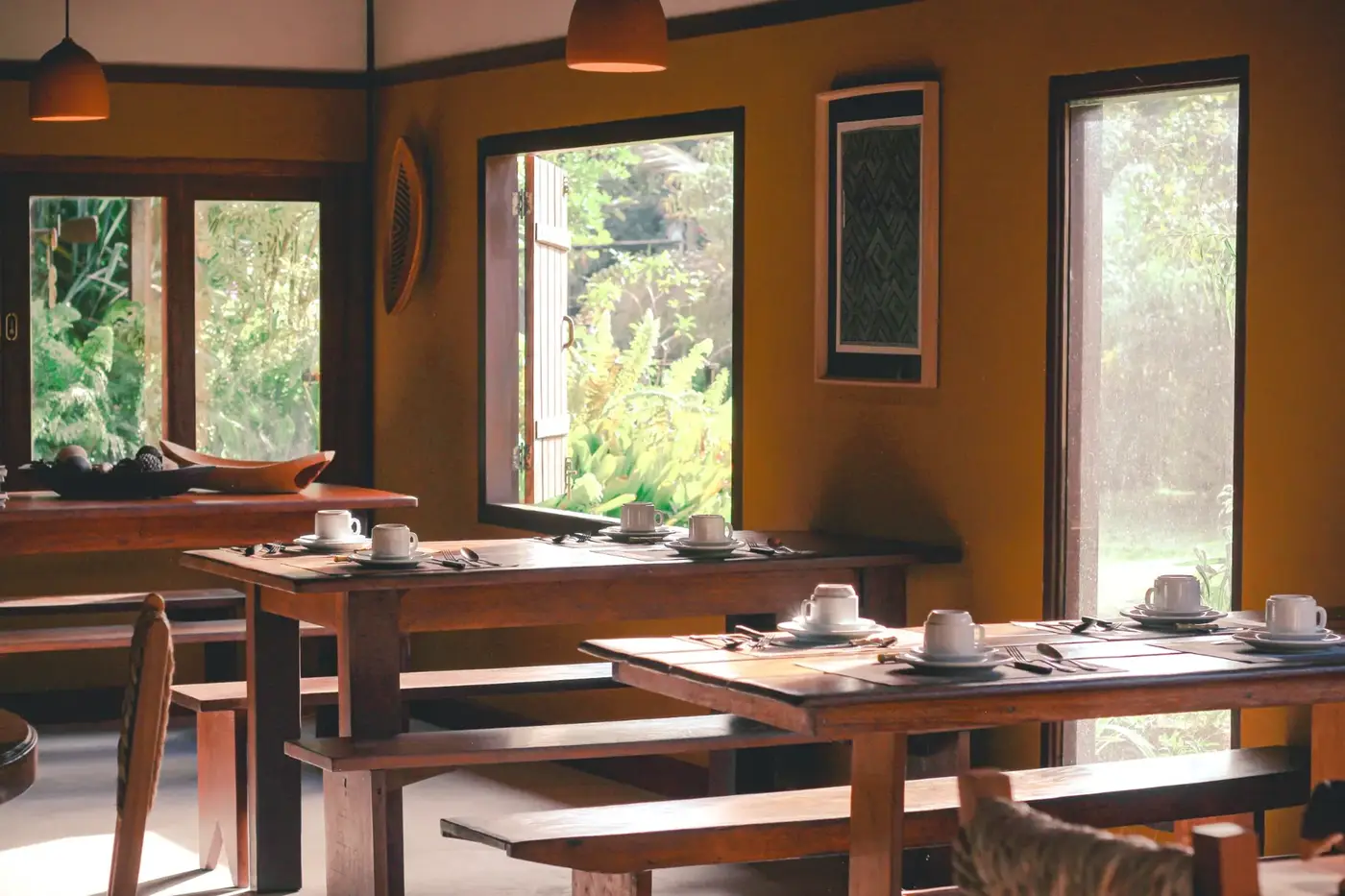 Salão de café da manhã com mesas de madeira e janelas para os jardins