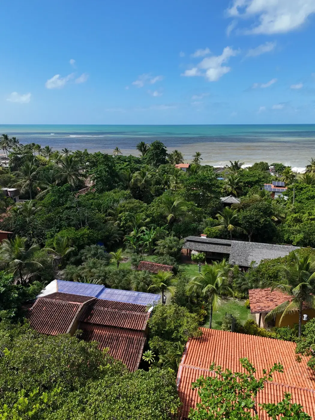 Vista aérea atual da Pousada Terra entre jardins e árvores, com o mar de Caraíva ao fundo